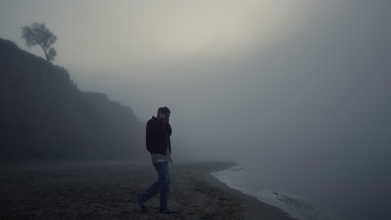 Casual guy wearing headphones on beach. Relaxed man listening music in earphones