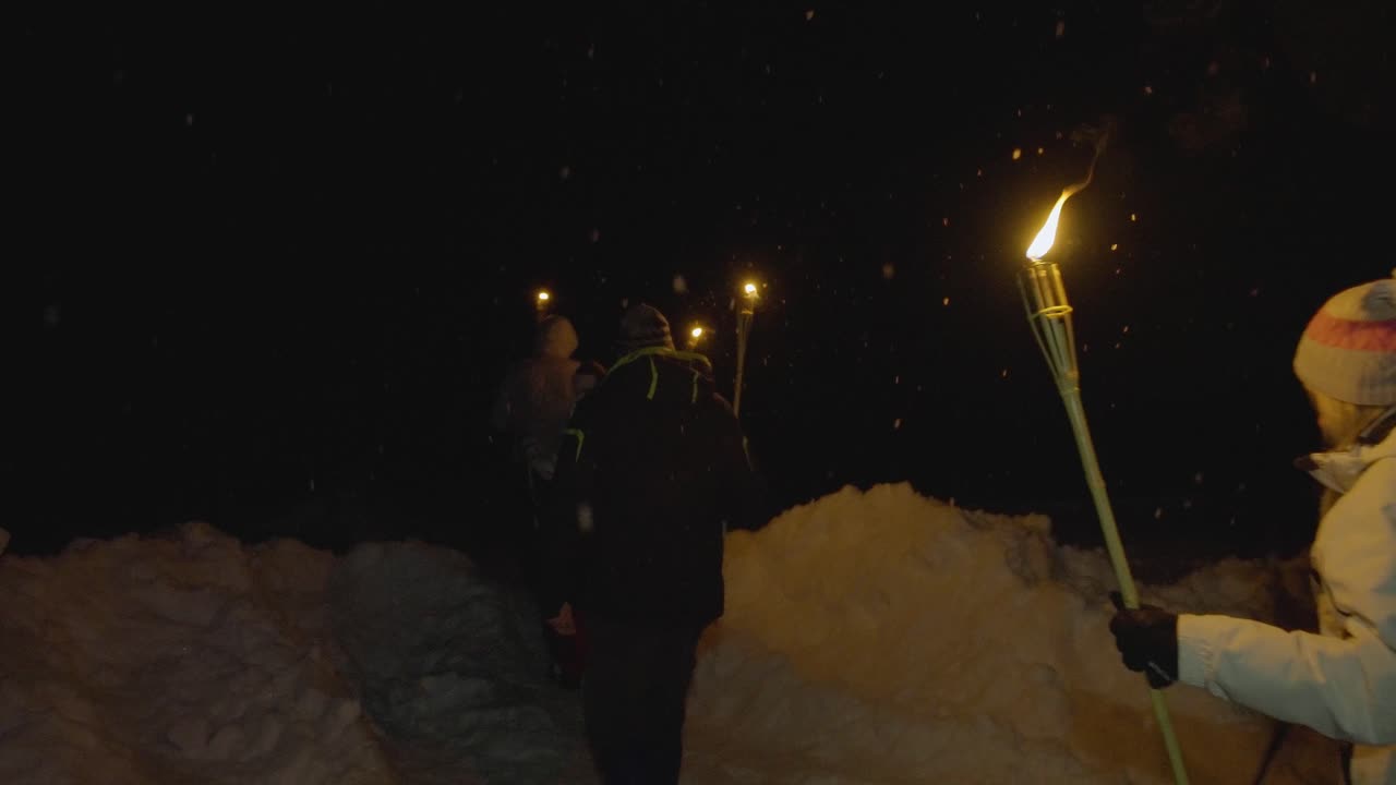people walking with torches at night time in a forest while it's snowing at wintertime captured in 4k with nature covered in snow