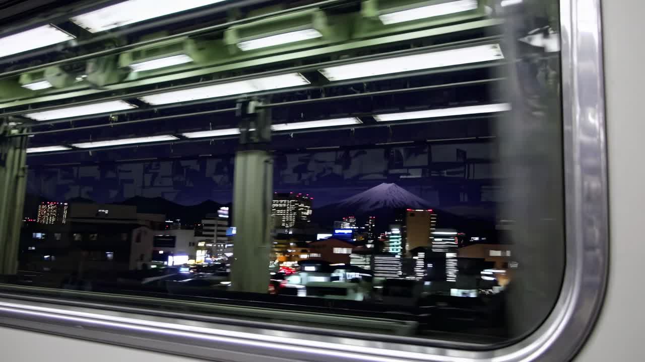 電車の窓から見た夜の街並み。都市の光と遠くの山々を捉えている