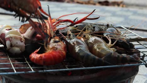 a side view of prawns, shrimps grilled on the barbeque , some of them are already cooked while others are raw, a girl is turning their to avoid burning