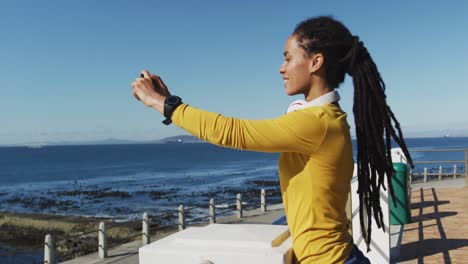 african american woman using smartphone on promenade by the sea