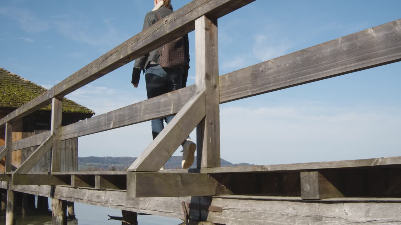 toma de seguimiento de una mujer caminando por un embarcadero hasta una pequeña cabaña en un lago de montaña transparente y reflectante