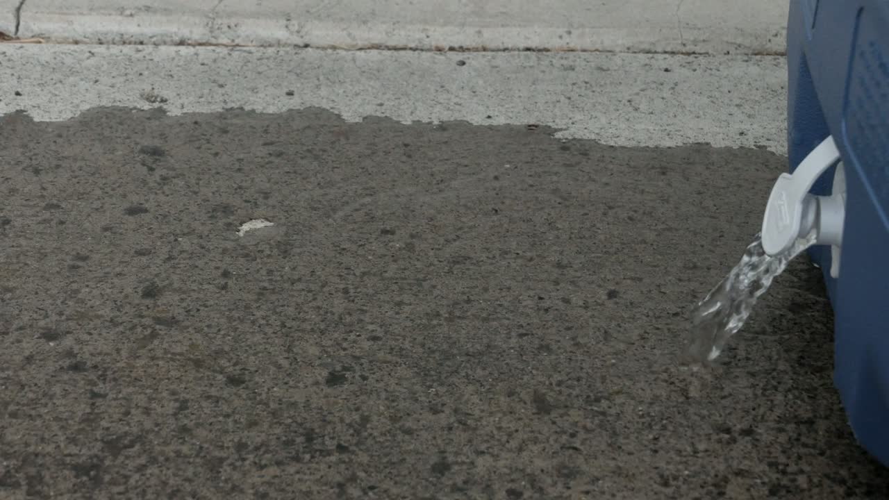 hand opening up a plug on a blue cooler to drain the water onto a concrete pad