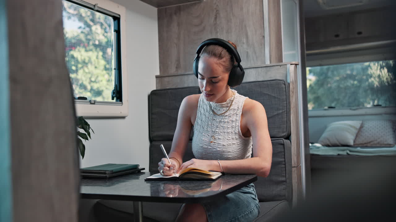Young Woman in Headphones Writing in Notebook Inside a Camper Van