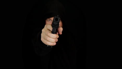 un hombre con una capucha negra caminando y disparando una pistola