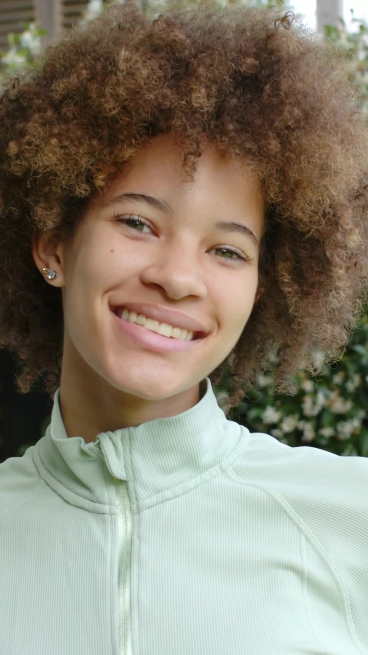Vídeo vertical: Mulher sorrindo virando-se para a câmera na varanda após sinal fora da tela, blusa de zíper verde-menta, postagem