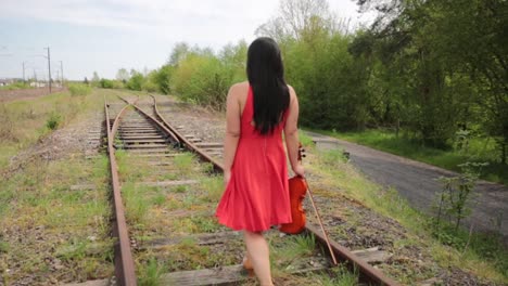 a young girl with red dress and violin walking on the rail