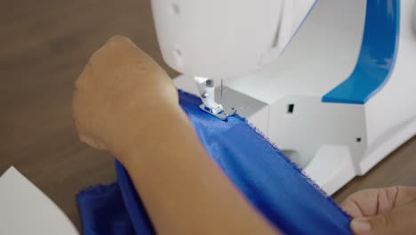 tailor's hands in closeup, sewing blue cloth with sewing machine