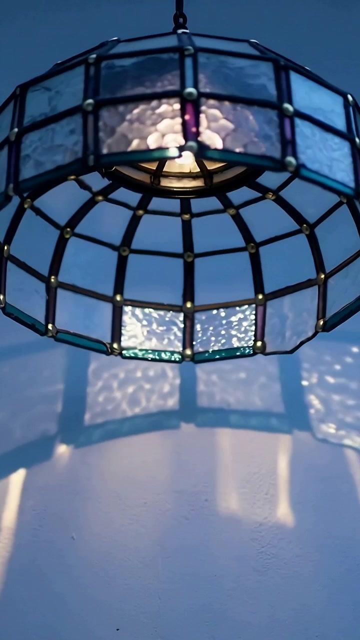 Video verticale: Telecamera che si muove, lampada in vetro colorato che proietta riflessi blu in movimento su un soffitto chiaro