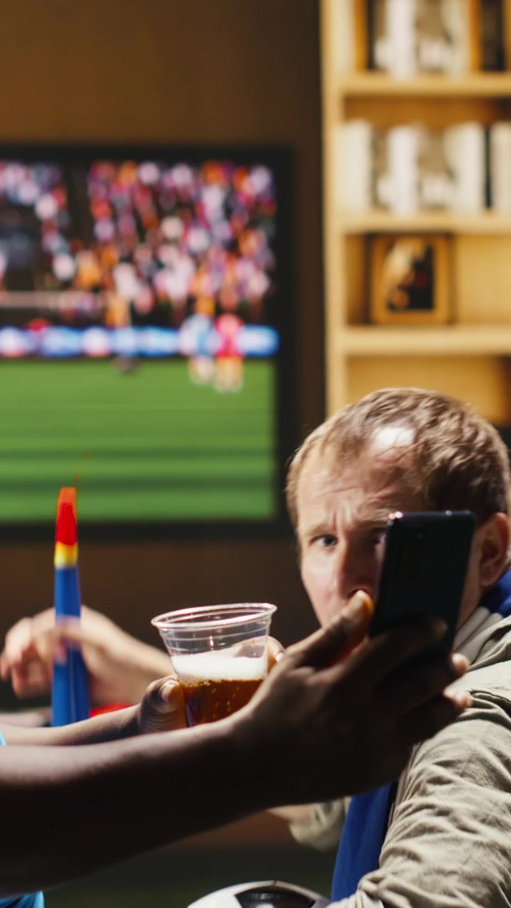 Vídeo vertical Homem no sofá segurando o telefone contando aos amigos sobre o resultado negativo do jogo de futebol