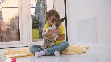 blond boy with curly hair sitting on the floor hugging his dog