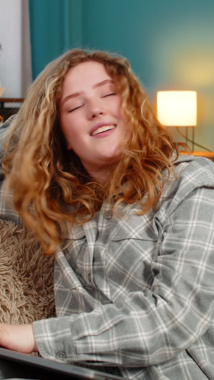 Young woman on sofa yawning stretching closing laptop after long work feeling happy and satisfied