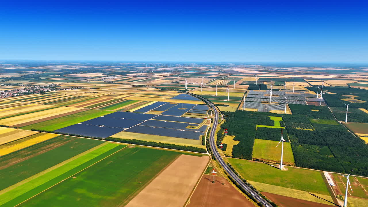 Vast fields and green energy. Aerial view of vast farmland and solar panels with wind turbines under a clear blue sky showcasing renewable energy