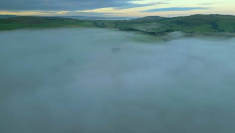 rising above misty fog bank revealing distant hills at sunrise