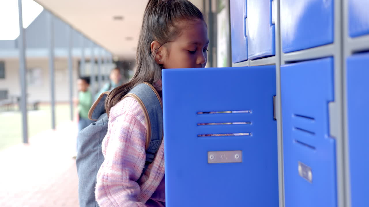 In school, young biracial girl with long black hair is opening her blue locker