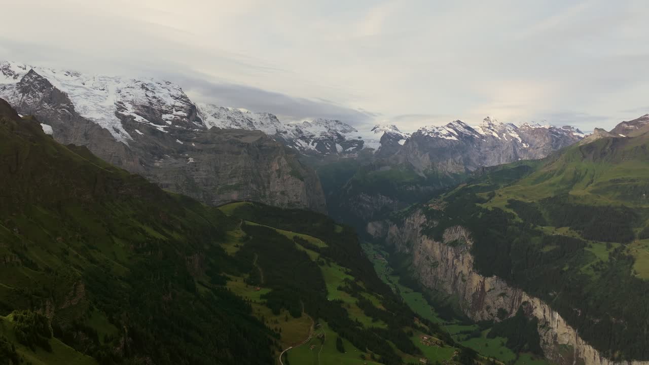 Aerial view of Lauterbrunnen Valley in Switzerland, showcasing dramatic cliffs, alpine meadows, and the towering snow-covered peaks of the Bernese Alps