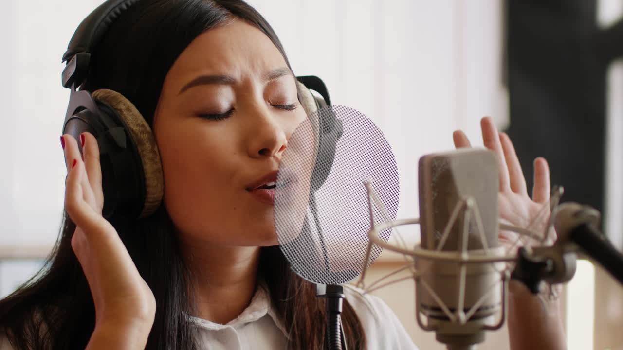 젊은 여성 이 녹음 스튜디오 에서 마이크 로 노래 하고 있다