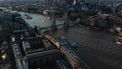 Tilt-up-reveal-of-Tower-Bridge-across-River-Thames-and-group-of-modern-office-buildings-in-City-financial-hub-in-golden-hour.-London,-UK