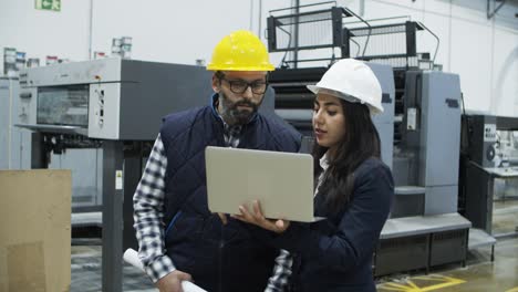 focused factory workers talking while standing with laptop