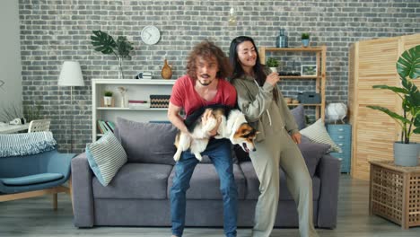 joyful guy dancing with girlfriend holding corgi puppy having fun at home