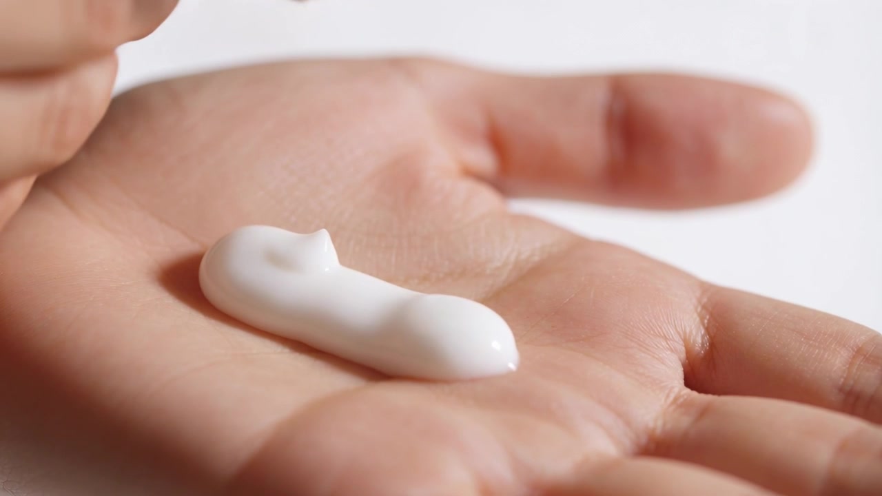 Eine Plastiktube wird gedrückt, Hände geben weiße Creme auf die Handfläche im Studio und verteilen sie zum Eincremen.