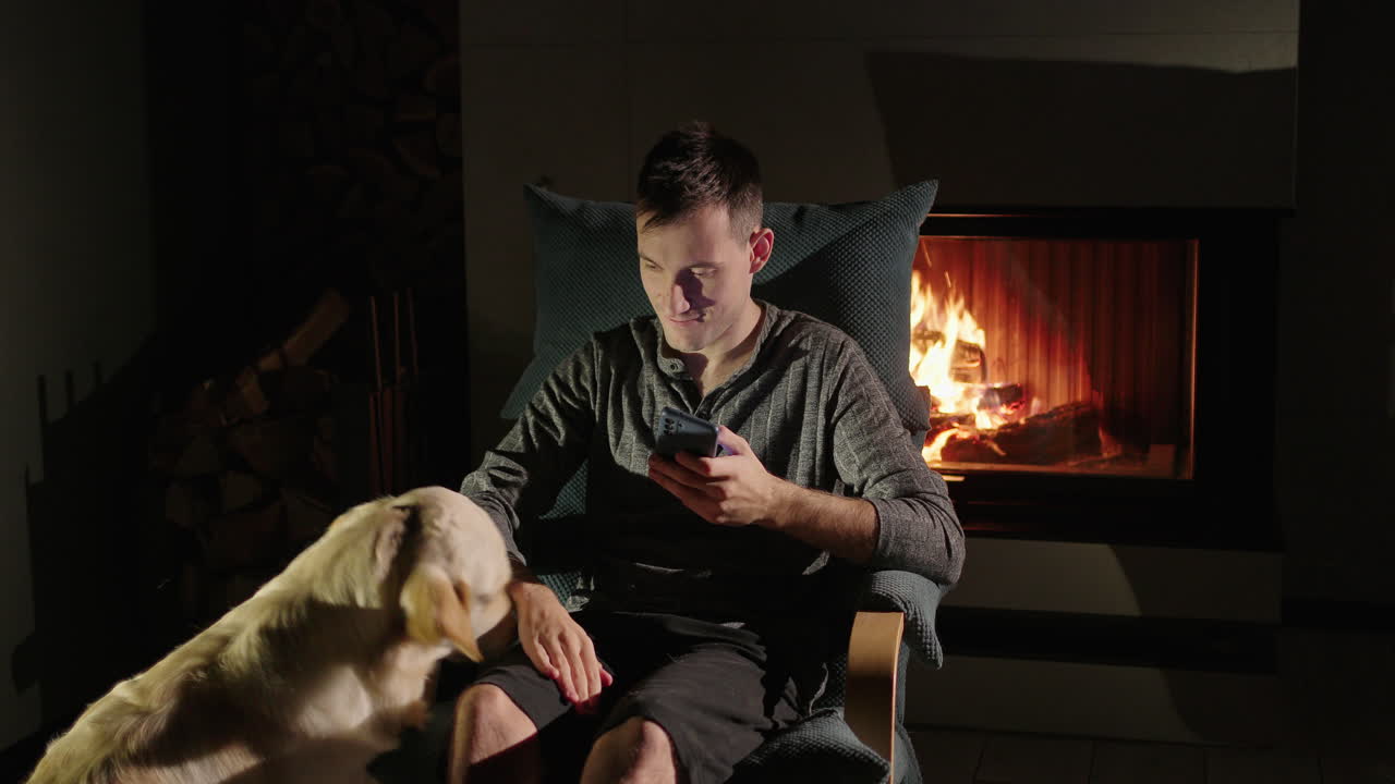 개 와 전화 를 가지고 벽난로  에서 휴식 하는 사람