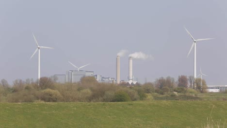 Panorámica-Desde-Un-Chorro-De-Agua-En-Un-Lago-Para-Revelar-Molinos-De-Viento-Y-Pipas-Industriales-Que-Muestran-Los-Cambios-De-Las-Tecnologías-De-Energía-Antiguas-A-Las-Nuevas