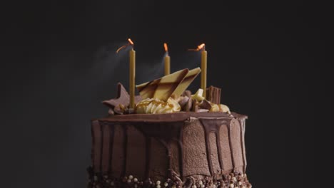 primer plano de estudio de pastel de celebración de cumpleaños de chocolate decorado con velas que se apagan contra fondo negro