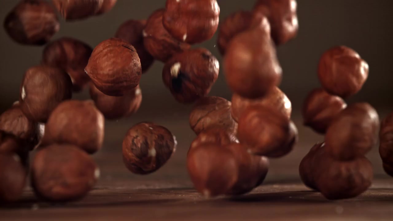 Nocciole sgusciate che cadono al rallentatore su una superficie di legno.