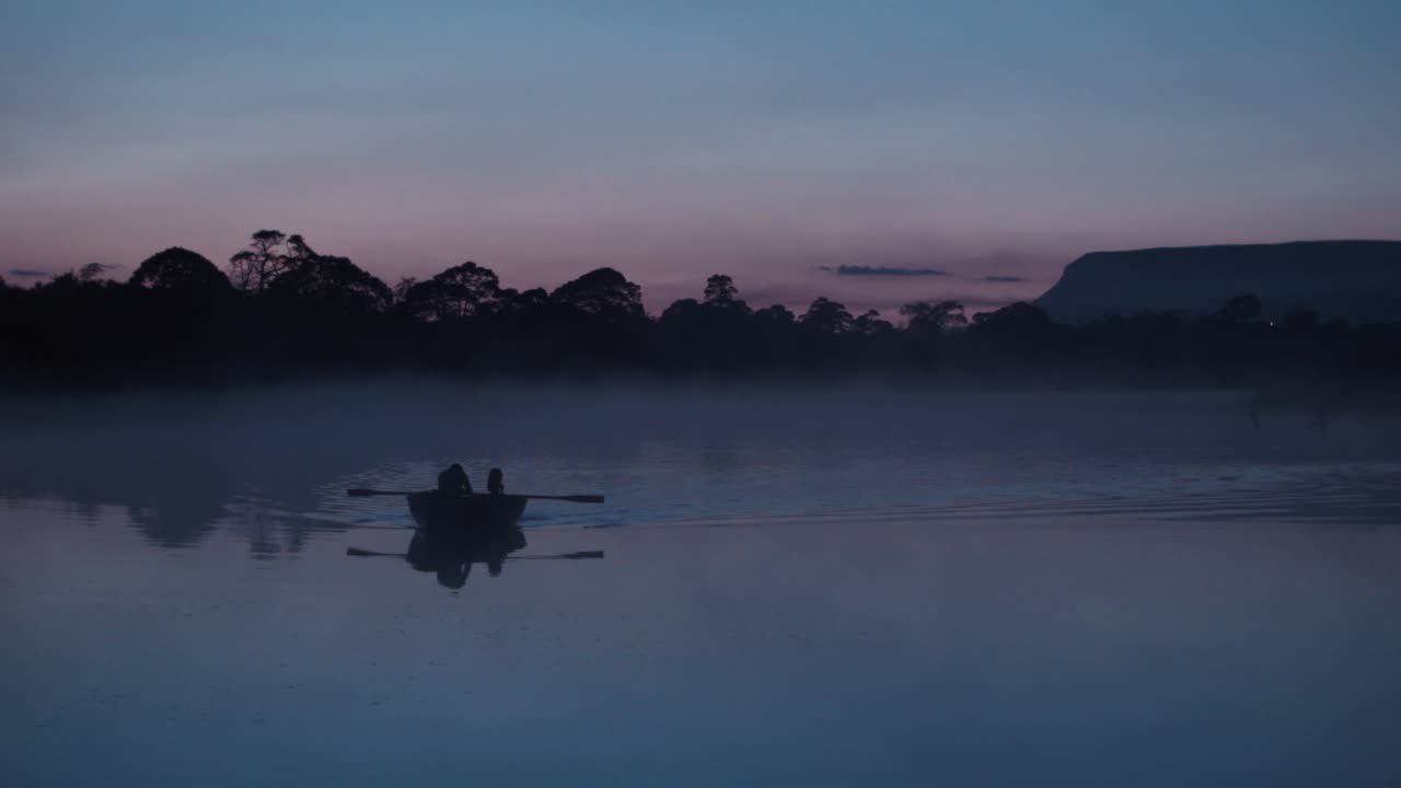 황혼에 안개 덮인 강에서 노를 젓는 활