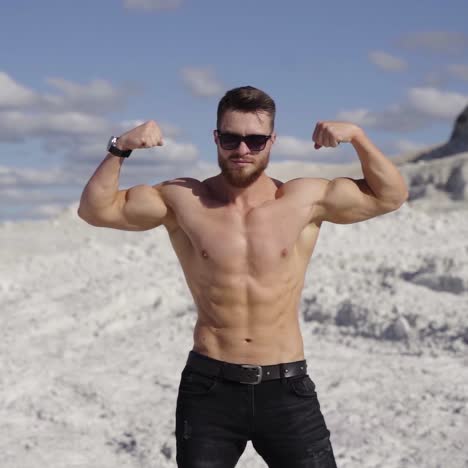 athletic man shows his muscular body outdoors. portrait of a shirtless sportsman with trained body on white canyon background in sunny daytime.