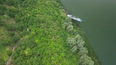 a slope that leads to the river filled with green trees towards the ship moored to the shore