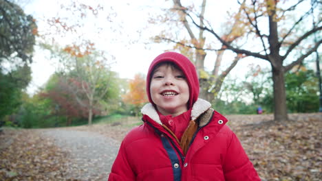 static view of a cute little boy smiling and posing for a shot wearing red jacket on the pathway by the side of the road on a wintry afternoon