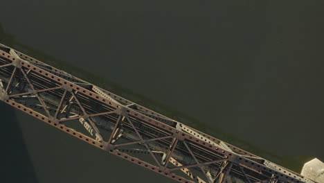 overhead ascending drone shot of a rail road bridge crossing a river captured at sunrise