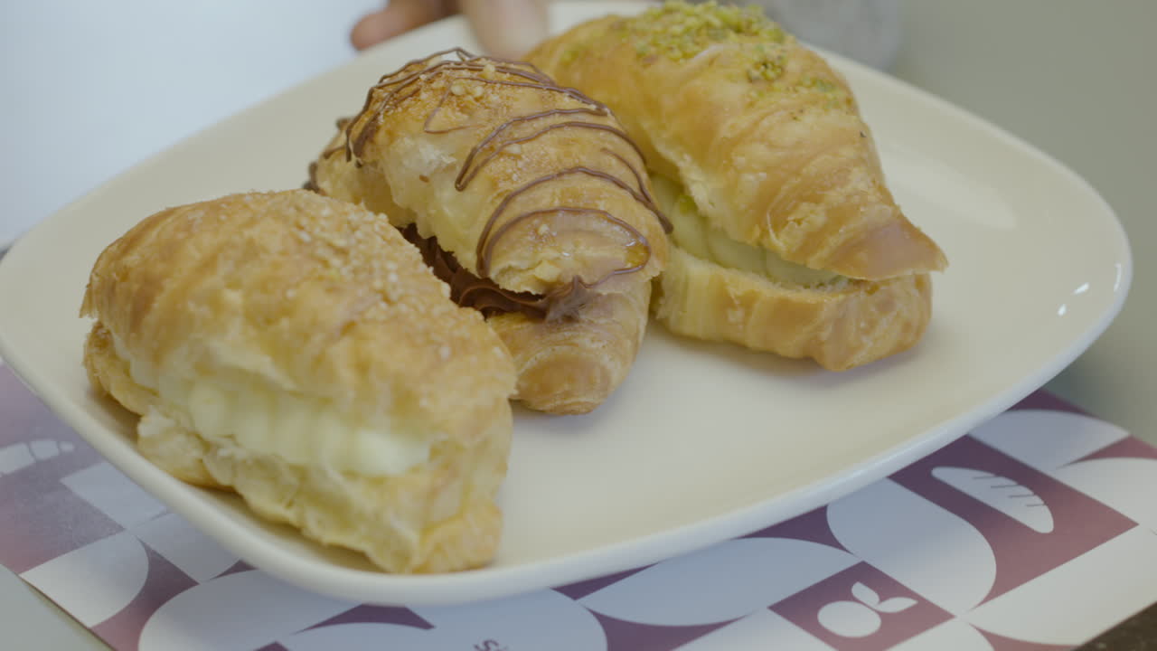 Close-up of three puff pastry croissants filled with cream, presented on a white plate. Golden, crispy and fresh texture