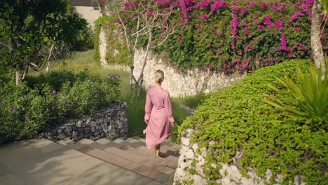 Woman-in-pink-kimono-walking-down-concrete-stairs-at-tropical-resort