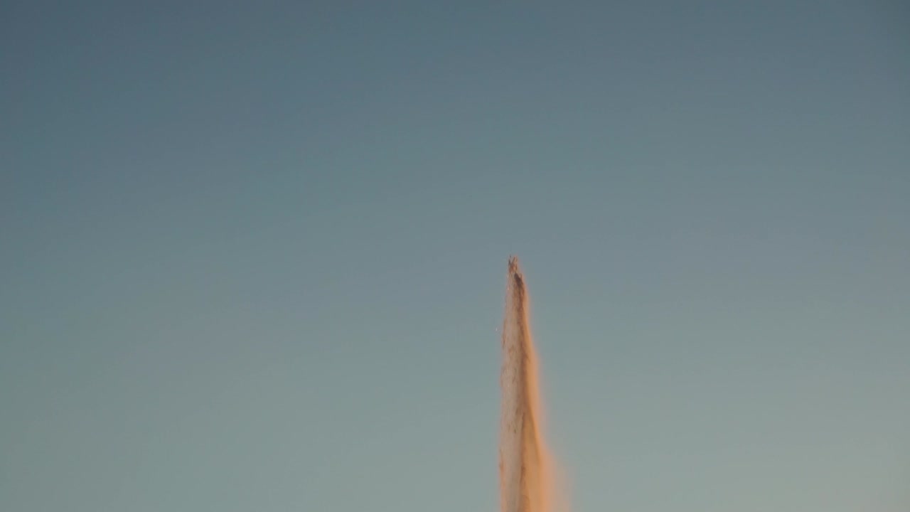 inclinación revela toma de fuente disparando al aire durante la puesta de sol, cámara lenta