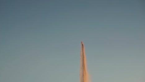 Tilt-reveal-shot-of-fountain-shooting-into-the-air-during-sunset,-slow-motion