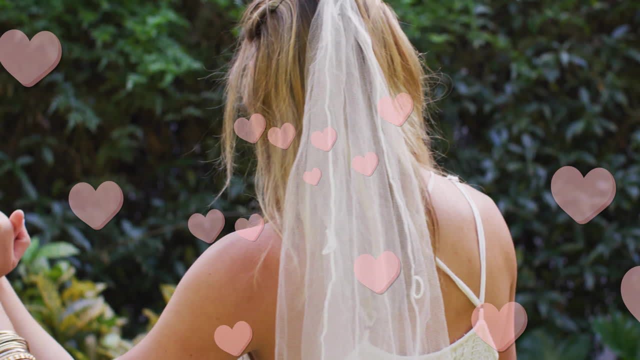 Animation of hearts floating over diverse female married couple dancing