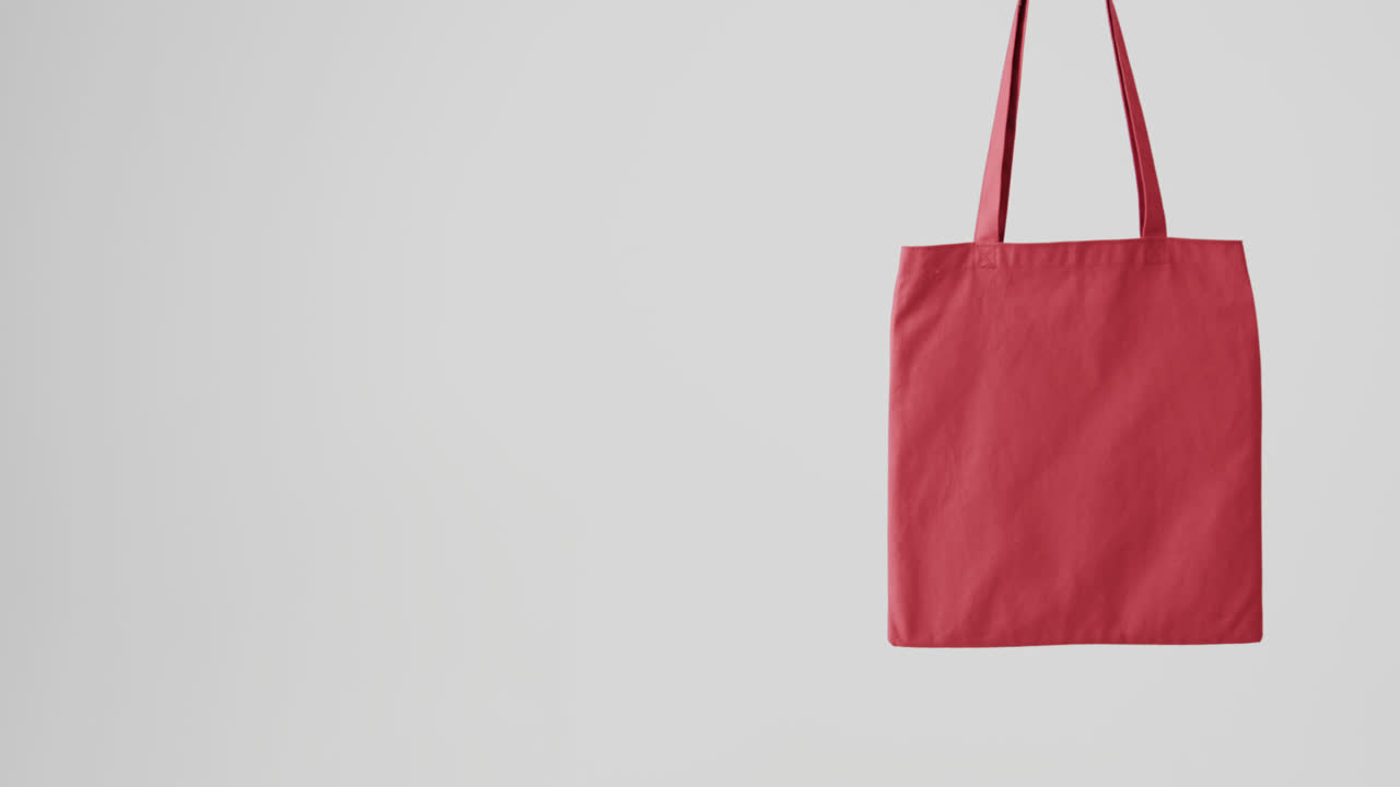 Mano de mujer caucásica sosteniendo un bolso rojo sobre fondo blanco, espacio para texto, cámara lenta.
