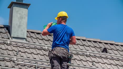 Young-thirsty-male-roofer-drinks-fresh-cold-water-out-of-green-plastic-bottle-on-hot-sunny-day