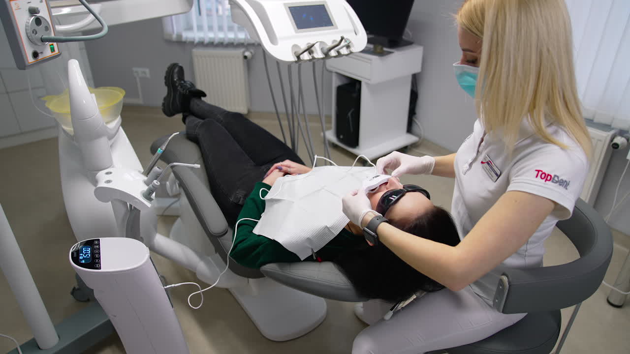 Young dentist at work in office. Woman laying on dental chair while dentist checking her teeth