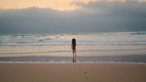 exotic model posing waves cloudy evening. woman walking on wet sand near ocean.