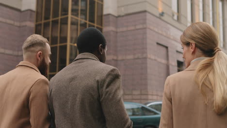 vista trasera de dos hombres de negocios caucásicos y africanos y una mujer de negocios caucásica hablando de su trabajo mientras caminan por la calle