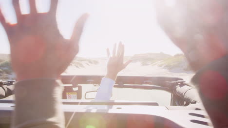 male friends in open top car with hands in the air, backlit