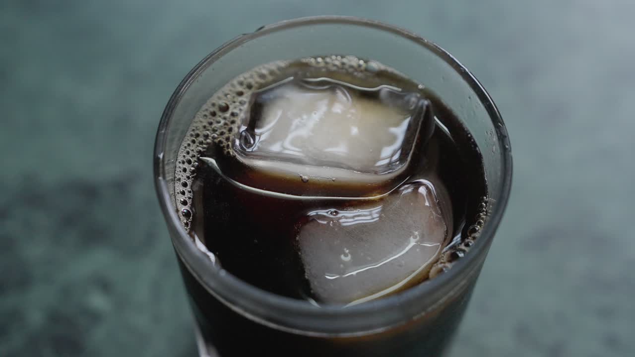 A close-up footage of stirring the ice cubes in an iced tea glass with a small stainless spoon, with blurred background