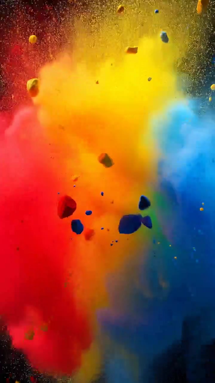 Primo piano che mostra un'esplosione concentrata di polvere colorata e frammenti di pigmento irregolari sospesi su uno sfondo nero, con un nucleo giallo al centro, una nuvola rossa a sinistra e una nuvola blu a destra.