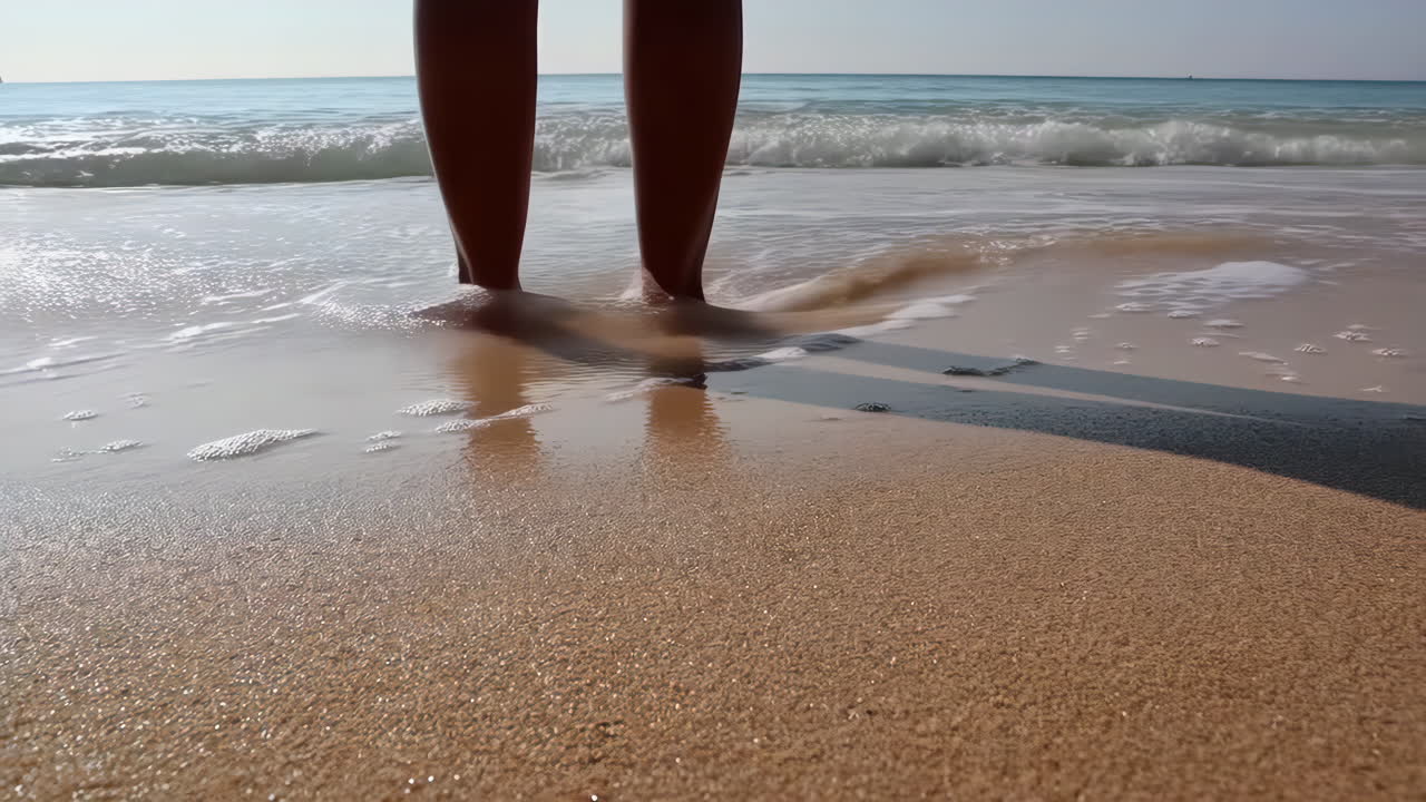 Legs standing in the ocean on a sandy beach with waves washing over them