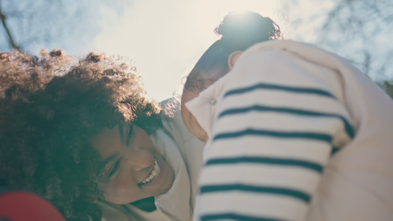 Laughing mother playing daughter outdoors at sunlight close up. Happy childhood.
