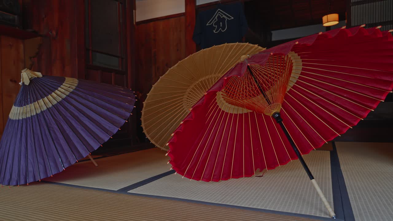 Una splendida ripresa interna che mostra ombrelli di carta oliata (Wagasa) rosso, viola e giallo vivaci esposti all'interno di un edificio tradizionale in legno all'Edo-Tokyo Open Air Museum.